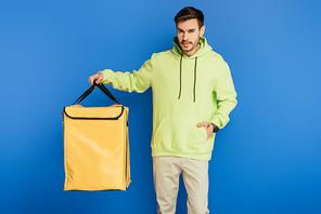 confident delivery man  while holding thermo backpack on blue background