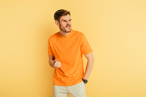 angry man grimacing and showing threatening gesture while looking away on yellow background