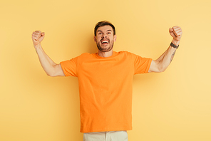 angry young man showing threatening gesture and grimacing while looking up on yellow background