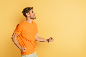 irritated young man showing threatening gesture and grimacing while looking up on yellow background