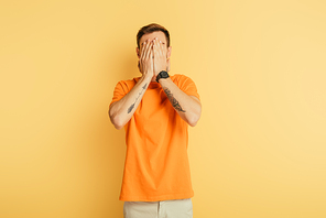 upset young man covering eyes with hands on yellow background