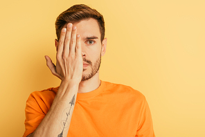 thoughtful handsome man covering eye with hand isolated on yellow