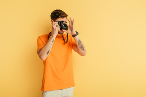 young tattooed photographer taking picture on yellow background
