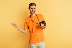 cheerful handsome photographer standing with open arm on yellow background