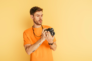 handsome attentive photographer looking at digital camera on yellow background