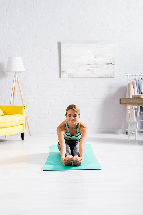 Smiling sportswoman stretching during yoga exercise on fitness mat
