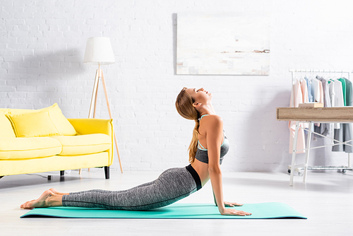 Woman in sportswear doing yoga asana with closed eyes on fitness mat