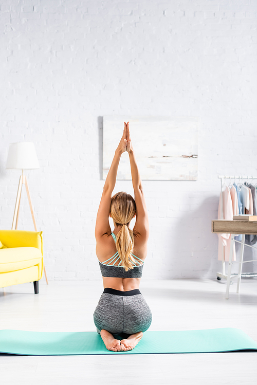 Back view of blonde woman sitting on fitness mat during yoga exercise
