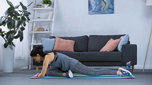 flexible young woman in sportswear stretching on fitness mat at home