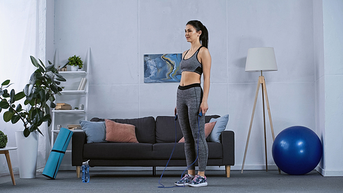 young woman in sportswear working out with jumping rope at home