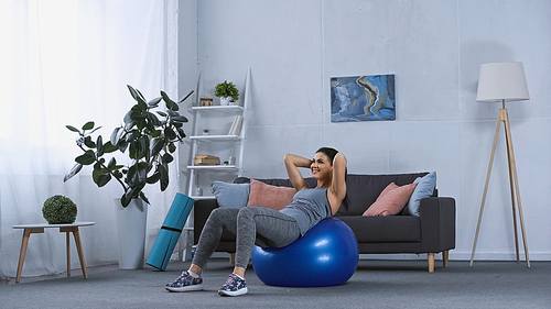 happy young woman in sportswear working out on fitness ball at home