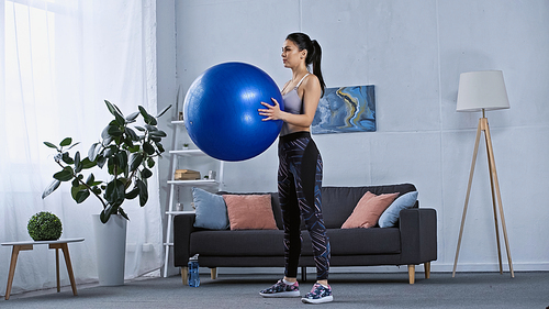 young woman in sportswear working out while holding fitness ball at home