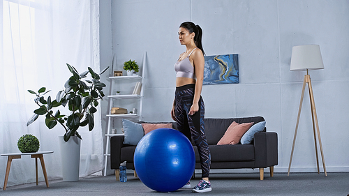 young woman in sportswear standing near fitness ball at home