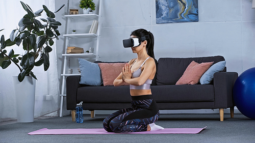 young woman in sportswear and vr headset sitting on fitness mat while working out at home