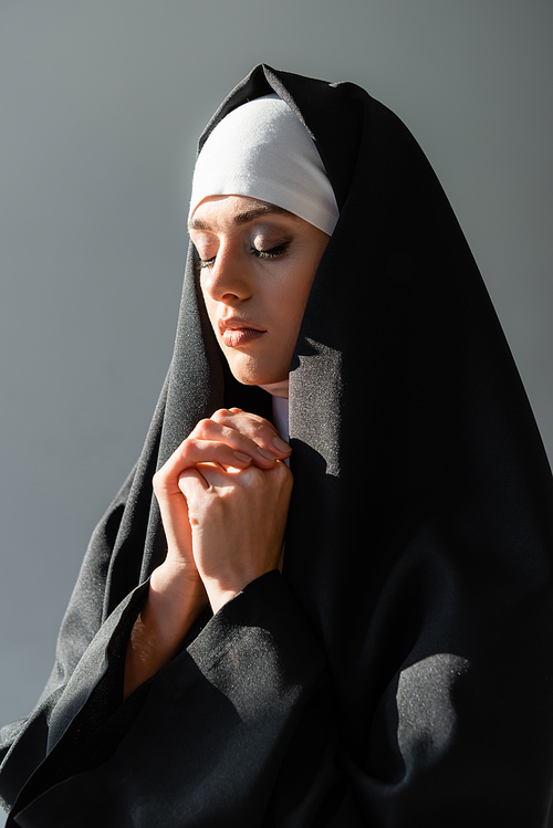 young nun praying with closed eyes isolated on grey