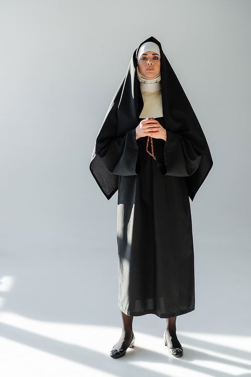 full length view of nun with crucifix  on grey background with shadows