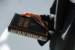 partial view of nun holding bible and prayer beads on grey background