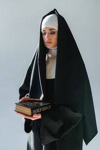 young nun in black cassock holding bible isolated on grey