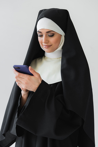 smiling nun chatting on smartphone isolated on grey