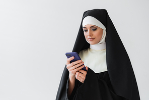 young nun in black vestment messaging on cellphone isolated on grey