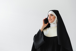 joyful nun in black mantle talking on mobile phone isolated on grey