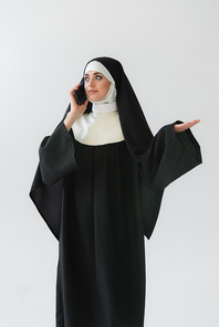 young nun in black vestment talking on smartphone isolated on grey