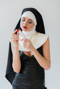 seductive nun in leather dress holding lighter isolated on grey
