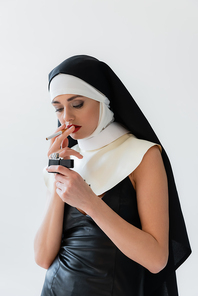 young nun in leather dress lighting cigarette isolated on grey