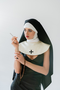 seductive nun looking away while smoking isolated on grey