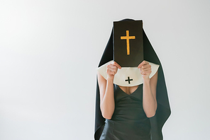 nun in sexy dress obscuring face with holy bible isolated on grey
