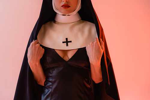 cropped view of sexy nun in black leather dress on pink background