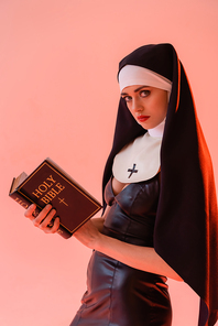 sexy nun in leather dress  while holding bible isolated on pink