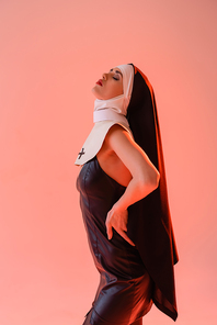 young nun in leather dress posing with closed eyes isolated on pink