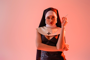 sexy nun in leather dress  while holding cigarette isolated on pink