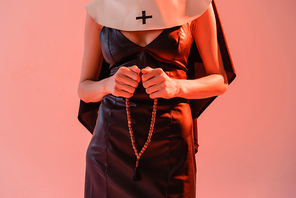 partial view of nun in sexy dress holding prayer beads isolated on pink
