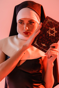sensual nun holding jewish bible isolated on pink