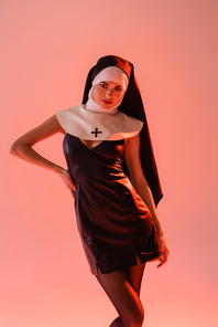 sexy nun in black leather dress posing with hand on hip isolated on pink