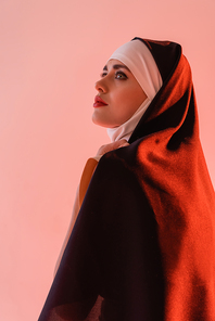 young nun in black vestment looking away isolated on pink