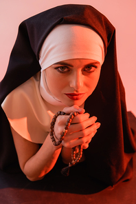 young nun  while holding rosary isolated on pink