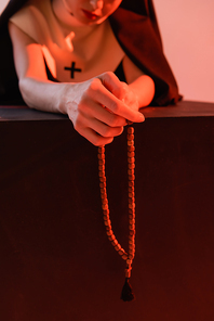 partial view of nun holding rosary isolated on pink, blurred background