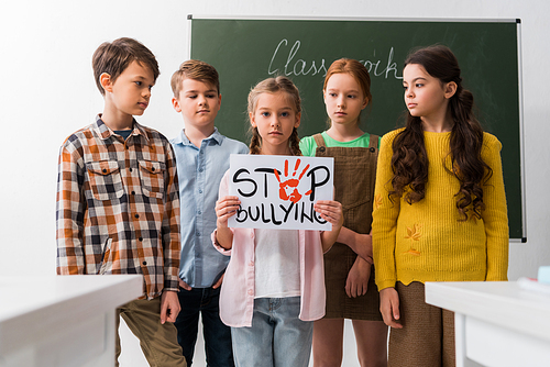 selective focus of schoolchildren looking at classmate holding placard with stop bullying lettering