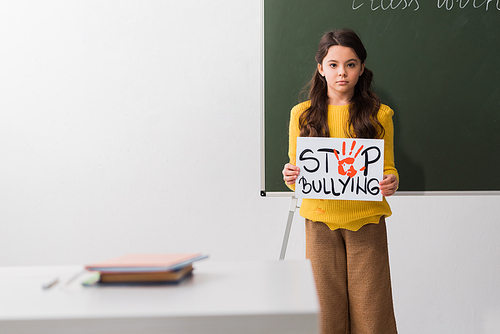 selective focus of schoolgirl holding placard with stop bullying lettering