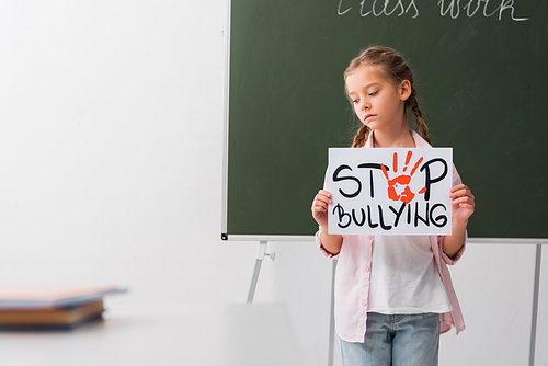 selective focus of sad schoolgirl holding placard with stop bullying lettering