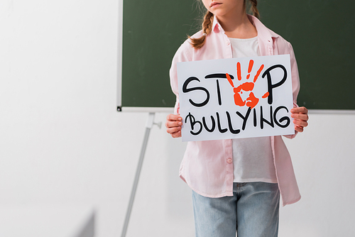 cropped view of sad schoolgirl holding placard with stop bullying lettering