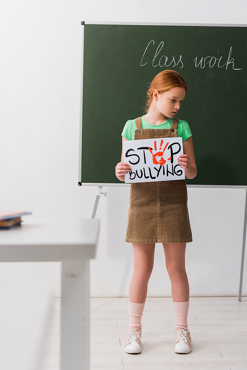 selective focus of cute schoolgirl holding placard with stop bullying lettering