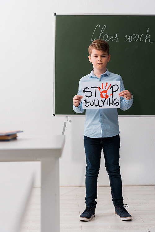 selective focus of schoolchild holding placard with stop bullying lettering in classroom