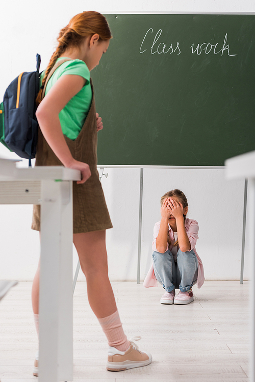 selective focus of schoolkid looking at crying classmate, bullying concept