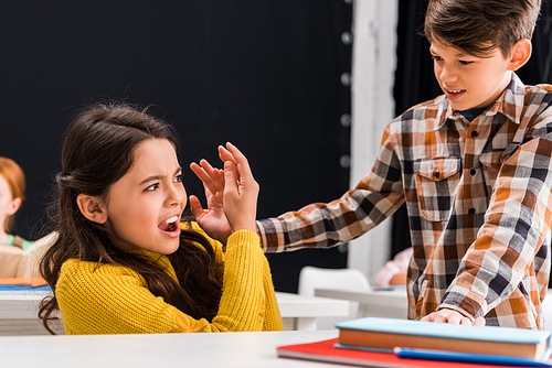 selective focus of cruel schoolboy abusing scared schoolgirl in classroom