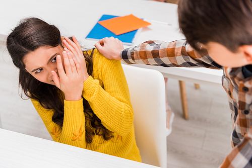 selective focus of cruel schoolboy bullying scared schoolgirl in classroom