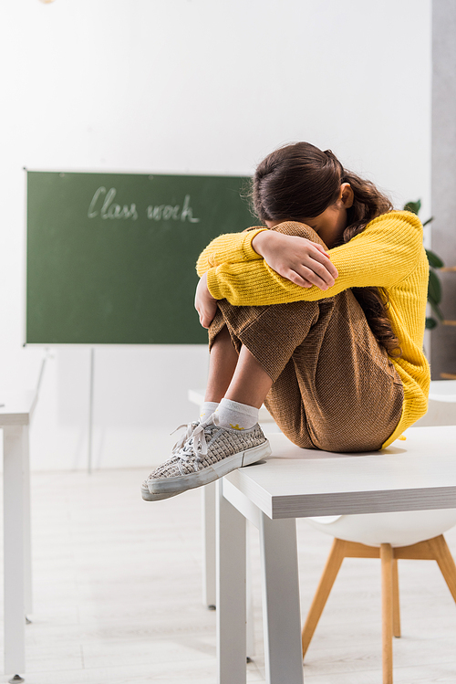 sad and bullied schoolgirl covering face while crying in classroom